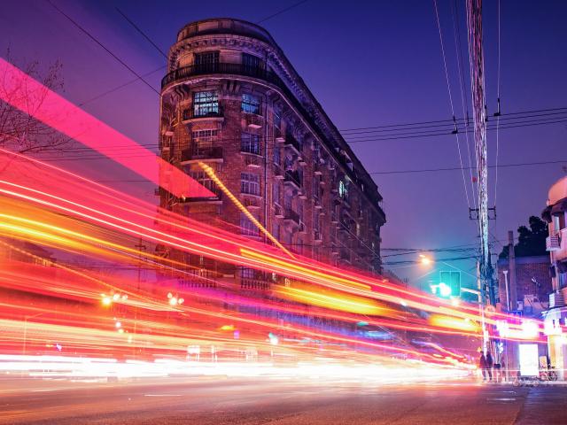 Bright, blurred lights from a vehicle move in front of a building